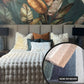 Bedroom with textured bedding and decorative pillows, featuring a close-up of a fabric with 'NOW OR NEVER' text.