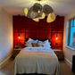 Modern bedroom with red upholstered wall panels, bed with pillows, and decorative lighting.