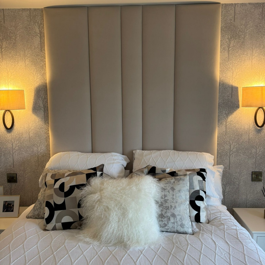 Decorative pillows on a bed with a upholstered headboard wall panels,  and lamps in the background