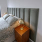 Wooden side table with lamp next to a bed with grey upholstered headboard