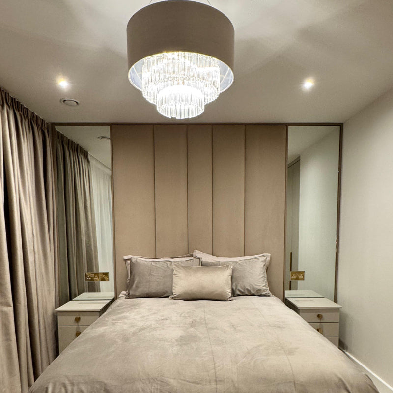 Modern bedroom with a large upholstered headboard, decorative pillows, and a chandelier.