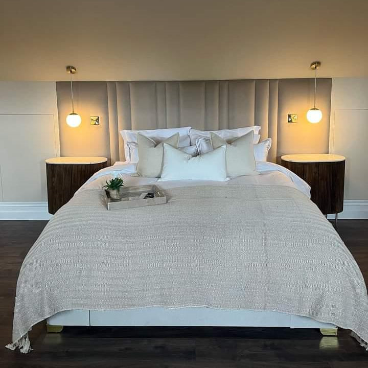 Neatly made bed with beige bedding in a bedroom setting and grey upholstered wall panels